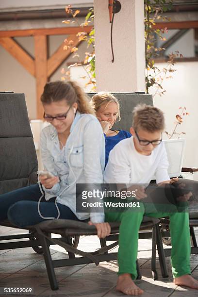 mother and her two children relaxing with digital tablet, smartphone and laptop on the terrace - 3 teenagers mobile outdoors stock-fotos und bilder