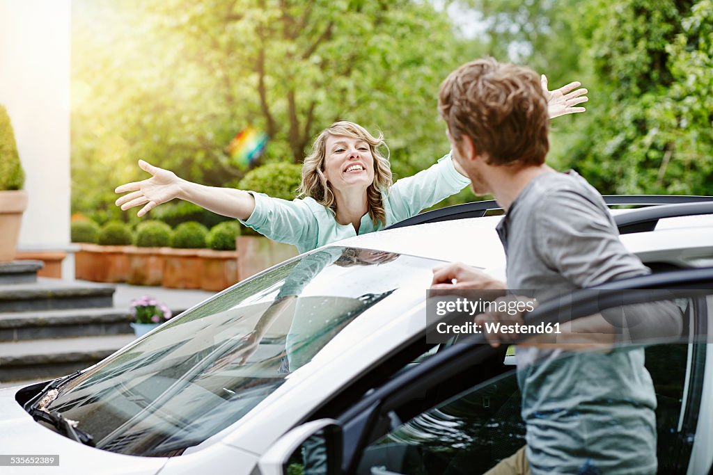 Happy woman with outstretched arms looking at man at car