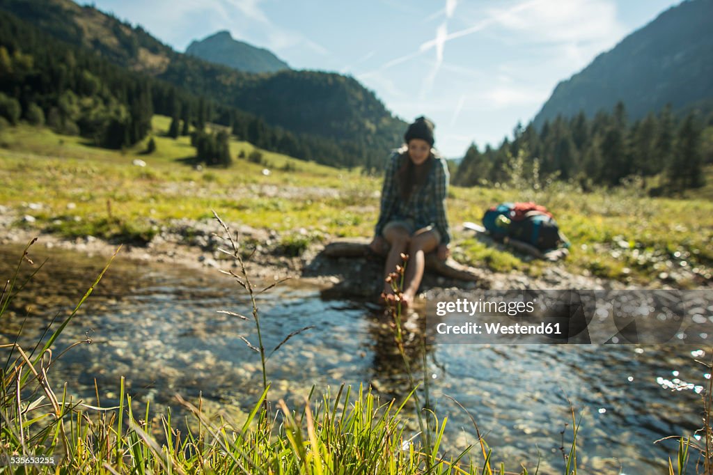 Austria, Tyrol, Tannheimer Tal, young female hiker relaxing at a brook