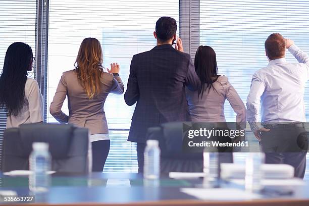 group of businesspeople looking through sunblinds in boardroom - private view stockfoto's en -beelden