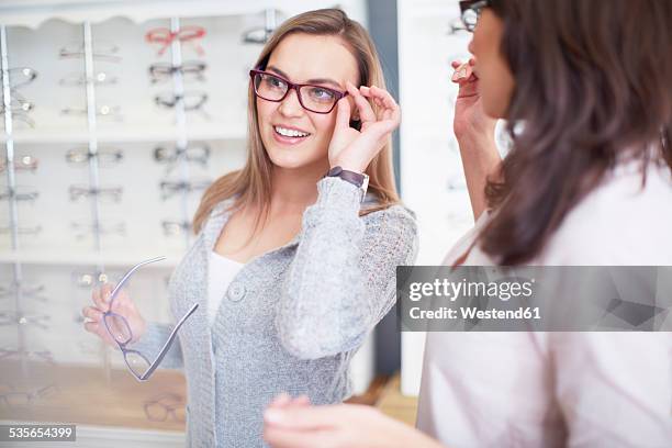 woman at the optician trying on glasses - optiker stock-fotos und bilder