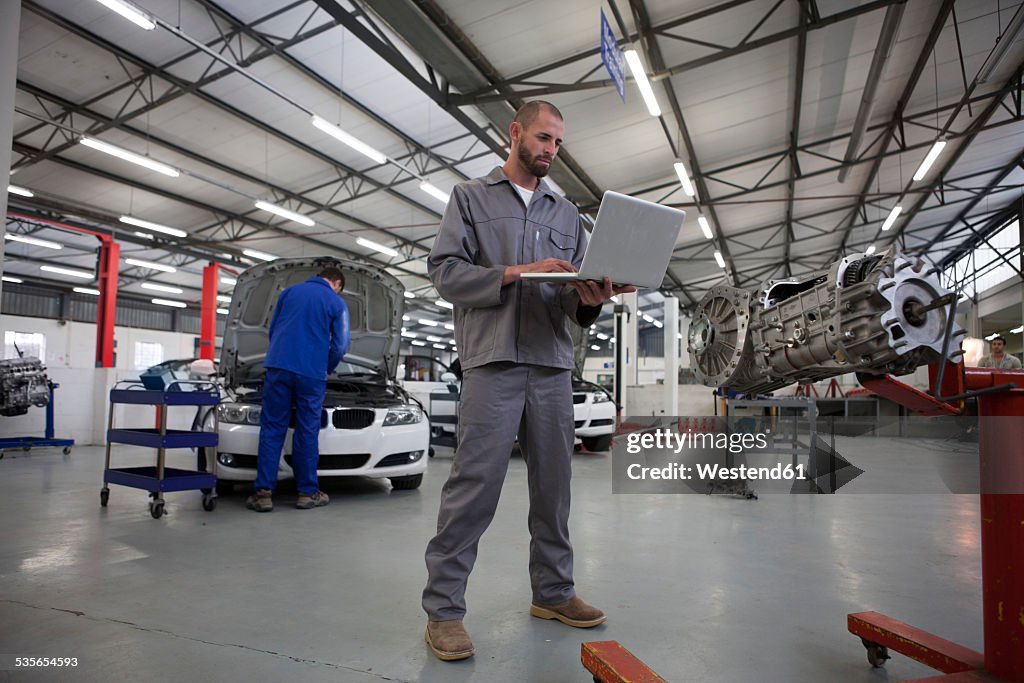 Two car mechanics with laptop in repair garage