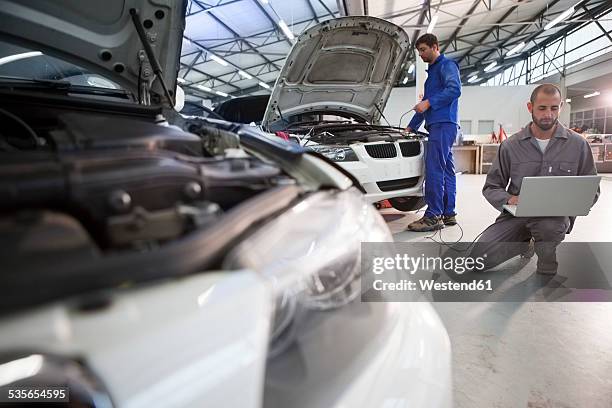 two car mechanics with laptop in repair garage - mechatronics stock-fotos und bilder