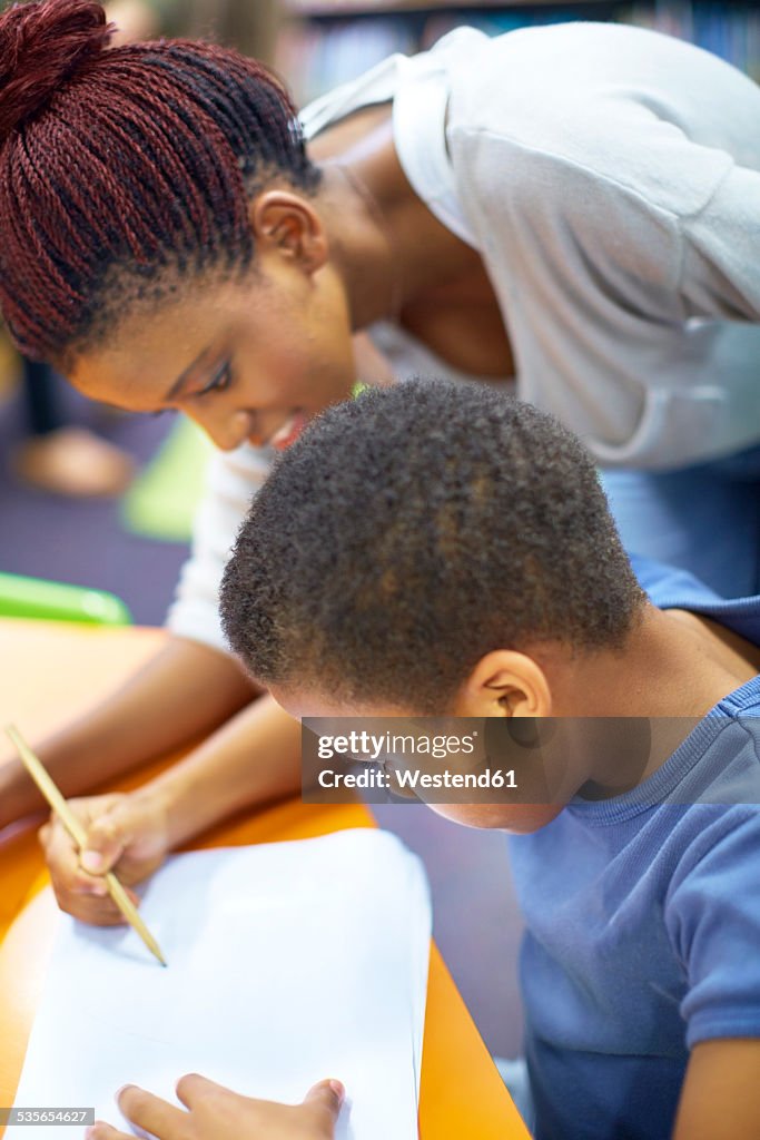 Young woman teaching boy writing on paper