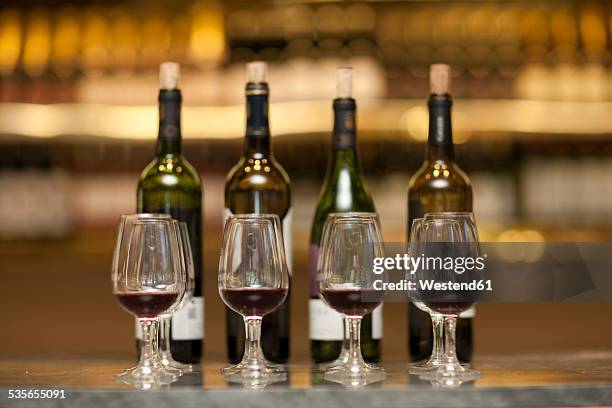 red wine glasses and wine bottles on a counter of a wine cellar - red wine tasting stock pictures, royalty-free photos & images