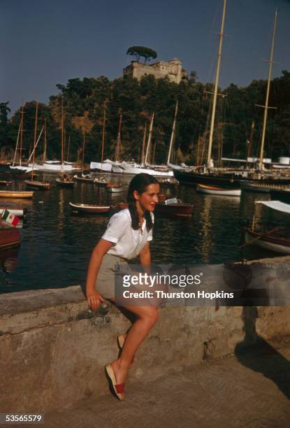 Young woman sitting on the harbour wall at Portofino on Italy's Ligurian coast, 1st December 1951. Original publication: Picture Post - 5599 -...