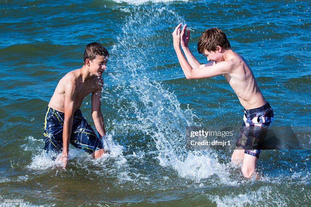 Two boys splashing water at each other in the ocean