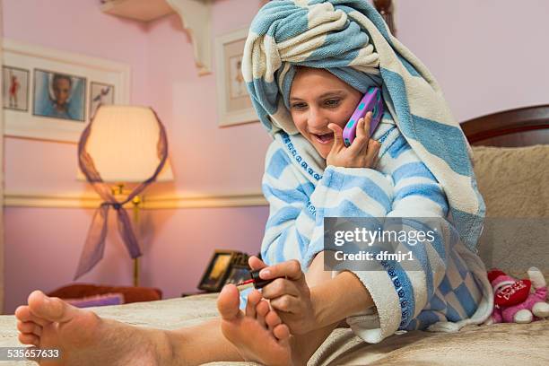 girl sitting on bed  talking on mobile phone while painting toenails - painting toenails stock-fotos und bilder