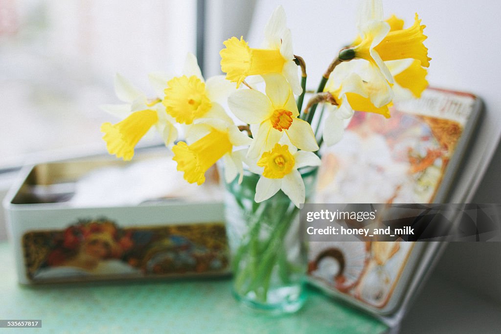 Yellow daffodils in a vase next to a tin