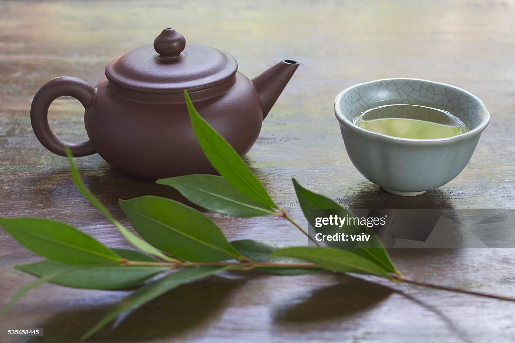 Still life with ceramic teapot, cup of green tea, and branch of tea plant