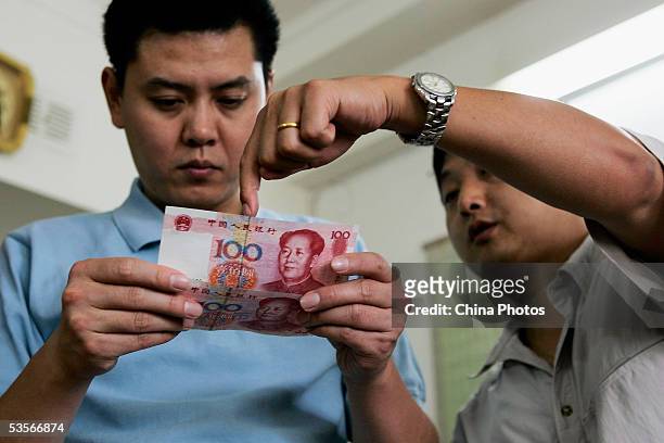 Bank clerk tells a customer how to identify a new issued 100 yuan note at a bank on August 31, 2005 in Shanghai, China. Authorities issued new yuan...
