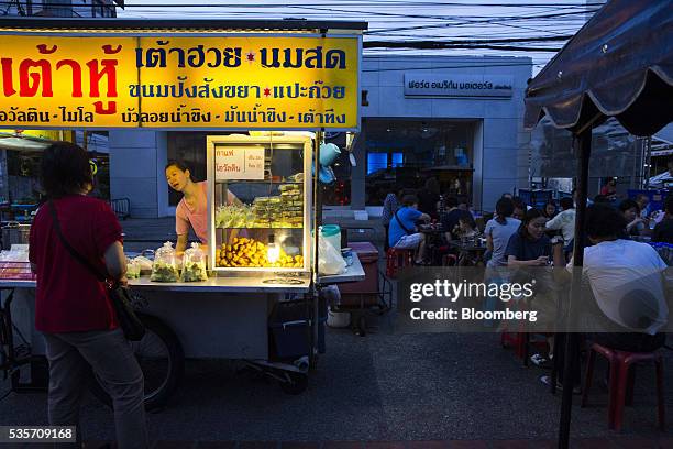 Vendor serves a customer at a food stall as diners sit at tables in the North Gate market in Chiang Mai, Thailand, on Sunday, May 29, 2016....