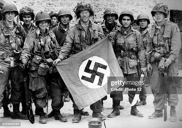 World War II, American paratroopers of an airborne division in Normandy, France, showing their spoil of war, a Nazi flag, June 1944.