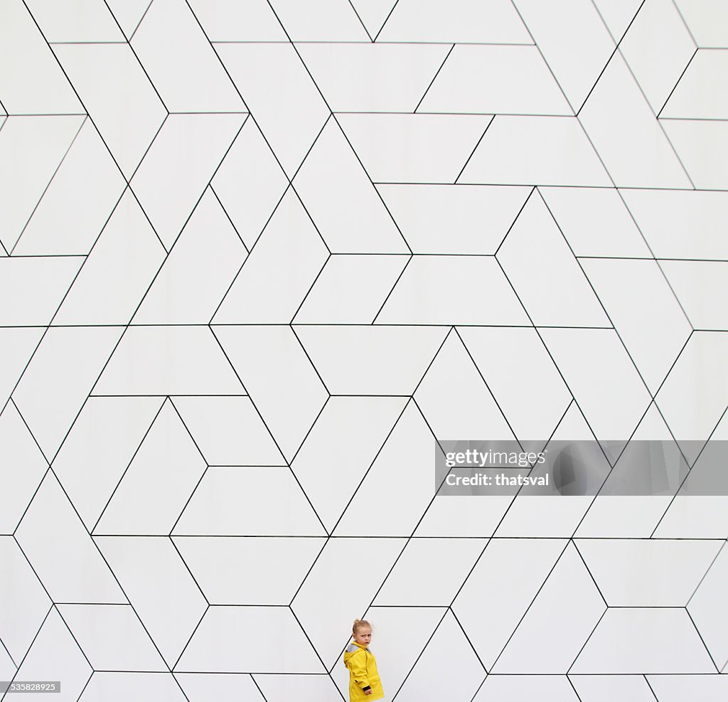 Girl (2-3) in yellow raincoat against white wall