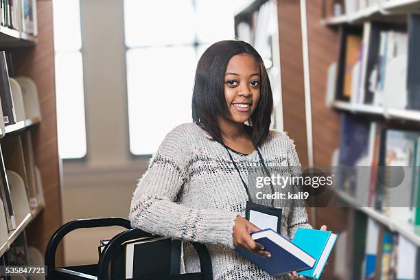 young woman refiling books on library shelf - librarian stock pictures, royalty-free photos & images