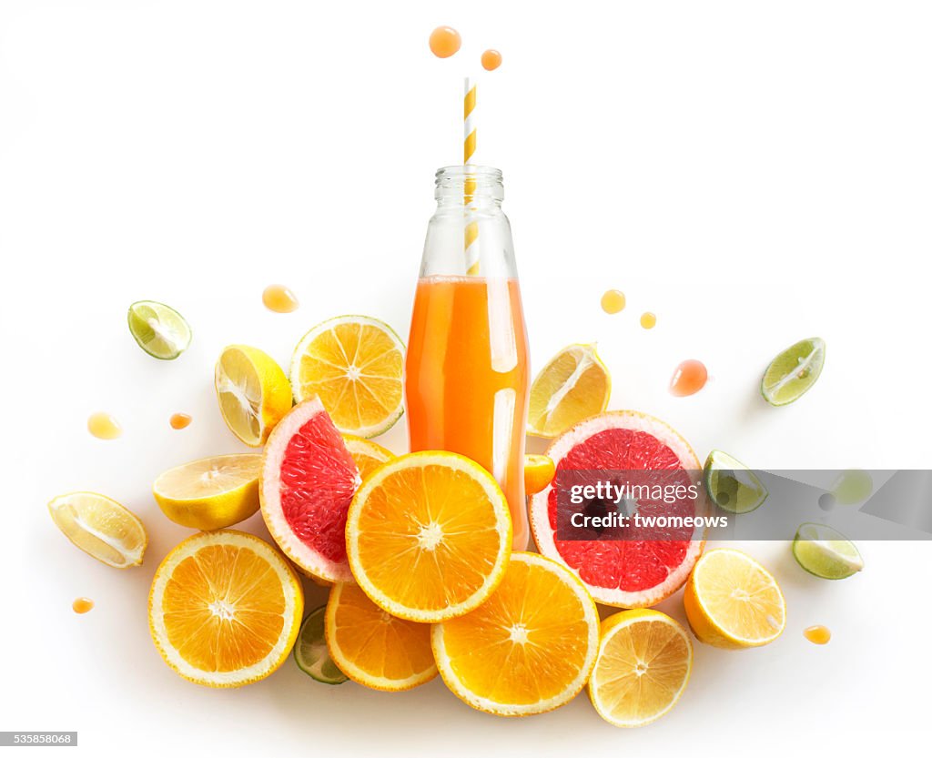 Bottled citrus juice with fresh citrus slices on white background. Juice flowing or splashing out from the bottle. Refreshing citrus juice design element.
