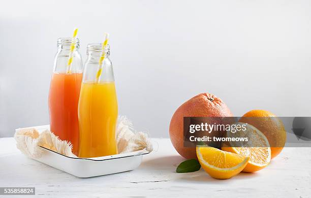 bottled citrus fruit juice with drinking straw along side with cut citrus fruits family stacked on white background. - fruits table top stock pictures, royalty-free photos & images