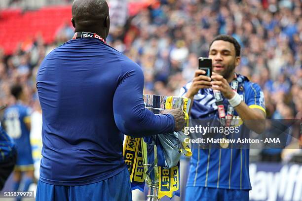 Adebayo Akinfenwa of AFC Wimbledon celebrates promotion by having his picture taken with the trophy by Andy Barcham after victory in the Sky Bet...