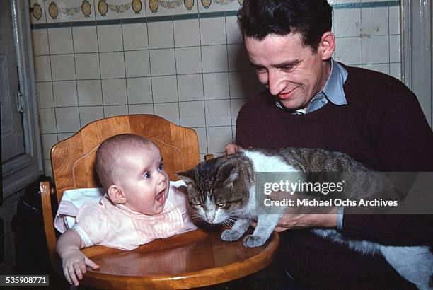 View of a truck driver, at home with his baby and cat, before driving a Mack Truck for Cooper Jarrett Motor Freight Lines in Illinois.