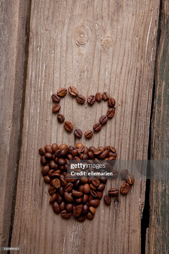 Coffee beans and cup with heart on wooden background