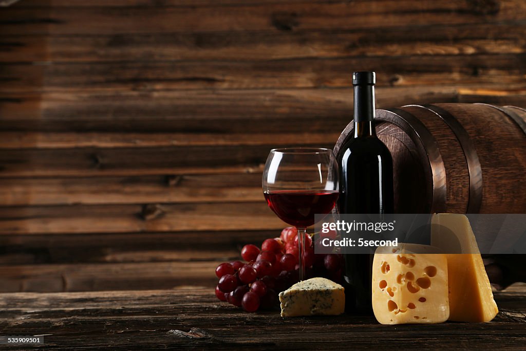 Glass of red wine, cheeses and grapes on wooden background