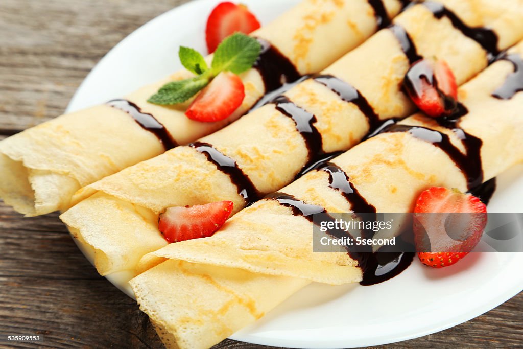 Rolled pancakes with strawberry on plate on grey wooden background