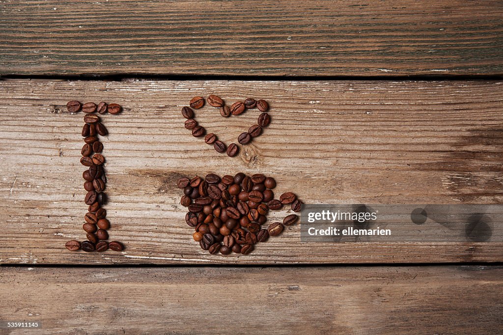Coffee beans and cup with heart on wooden background