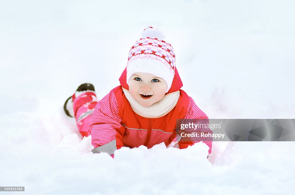 Funny child playing on the snow in winter day