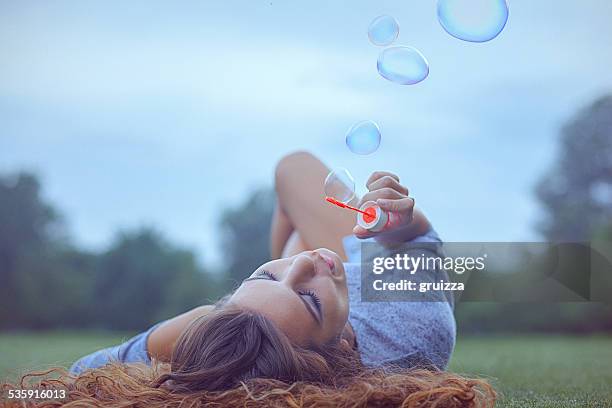 junge frau, die spaß und blasen blasen im freien - lying on grass stock-fotos und bilder