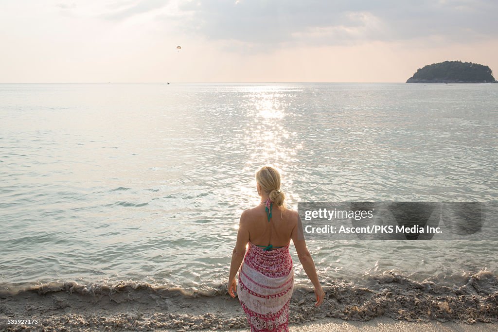 Woman walks along beach edge, looks out to sea