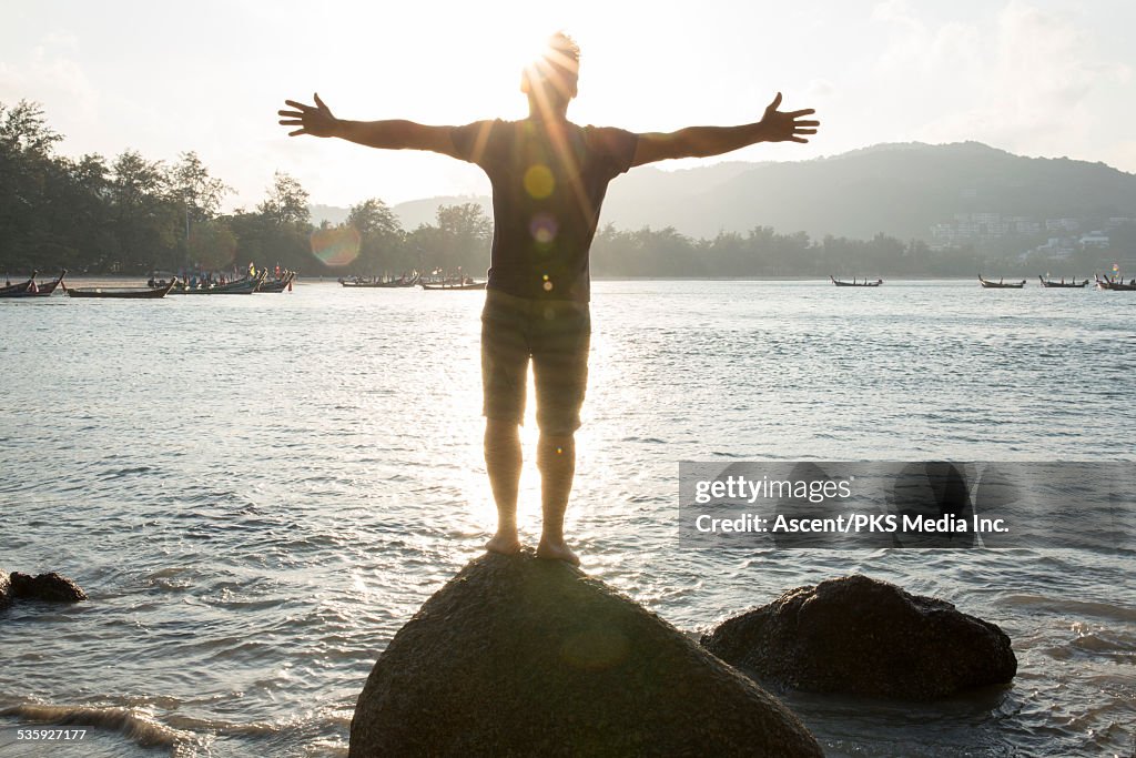 Man stands on rock overlooking sea, arms out