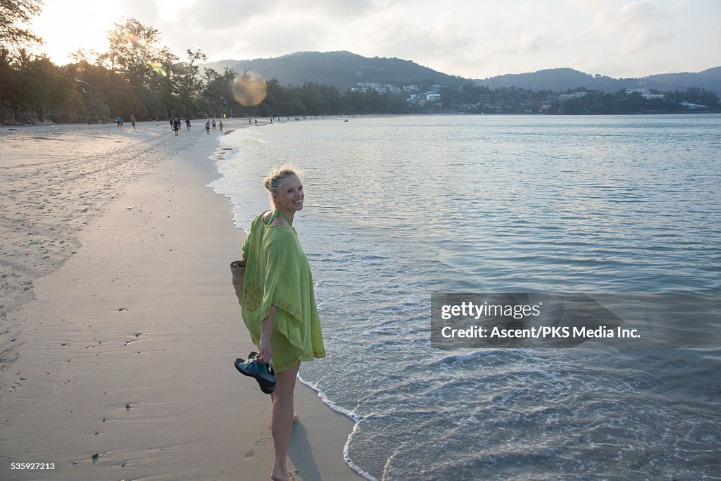 Woman strolls along beach, smiles back at camera