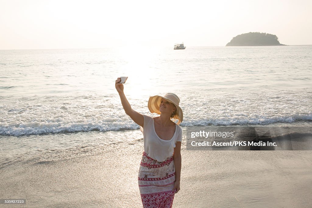 Woman takes selfie at beach edge, sunrise