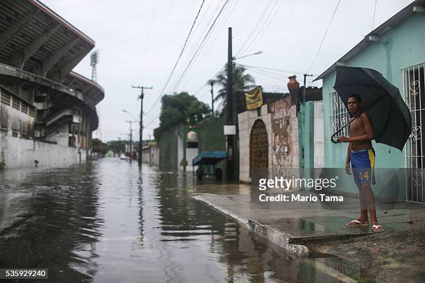 Young man stands with an umbrella along a flooded street after heavy rains on May 30, 2016 in Recife, Brazil. Lack of proper drainage in areas is one...