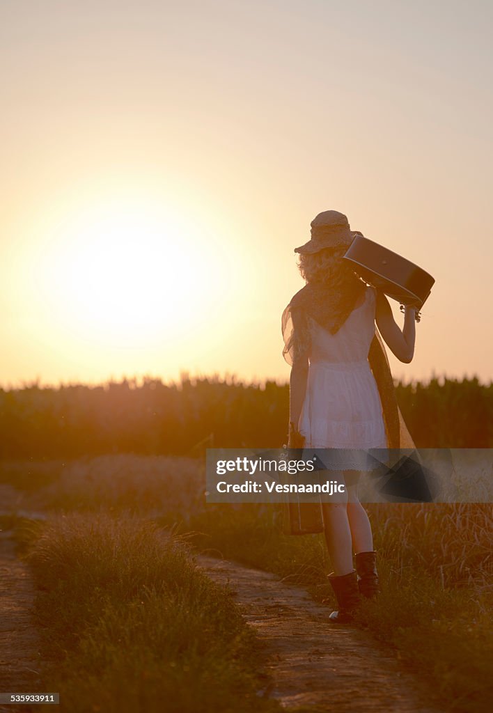 Woman with cello and suitcase in sunset