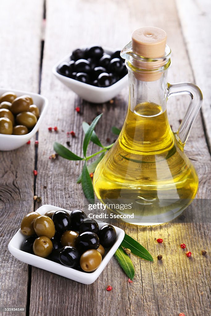 Green and black olives in bowl on grey wooden background