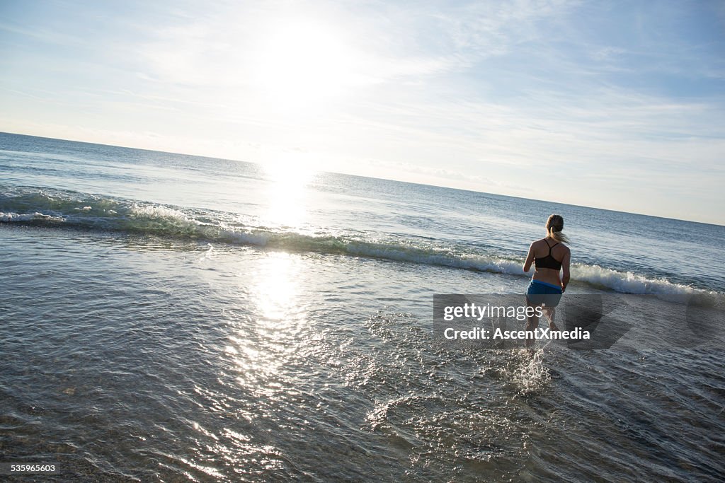 Teen girl runs across beach into waves, gentle surf
