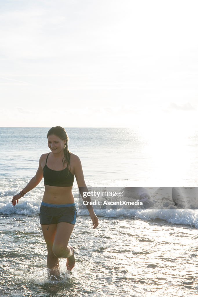 Teen girl walks up beach after swim, gentle surf