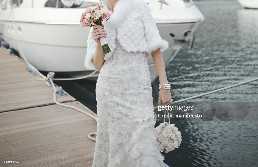 Novia con ramo pasos en el muelle ubicado cerca de yates.