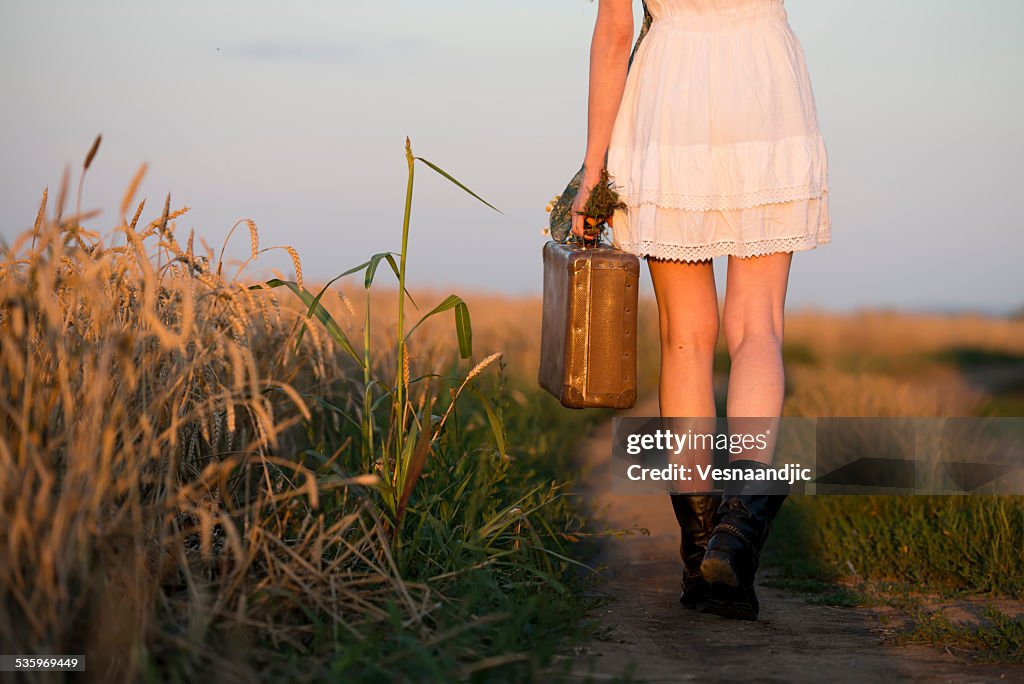 Woman in white dress and boots holding suitcase walking