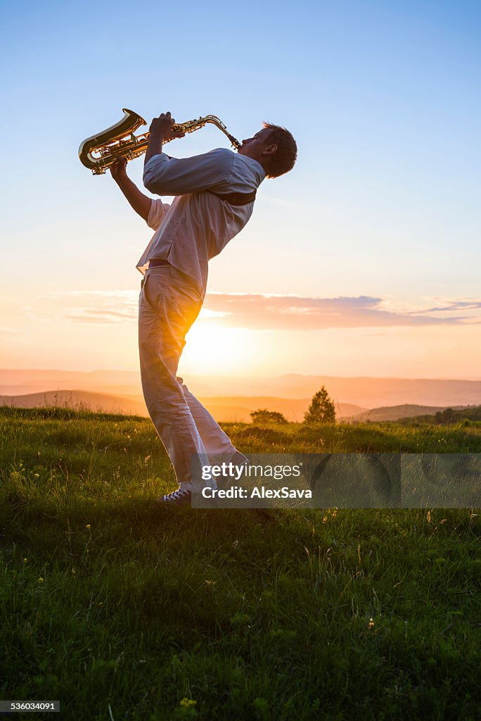 Young man playing saxophone outdoor at sunset
