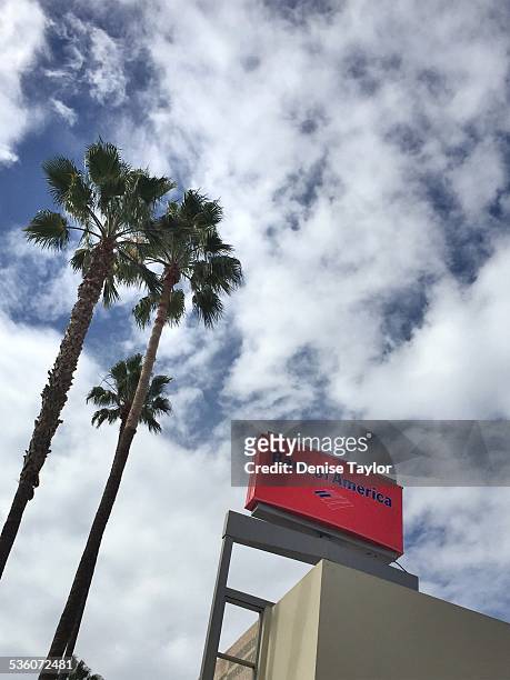 Red Bank of America sign against blue sky with clouds and palm trees
