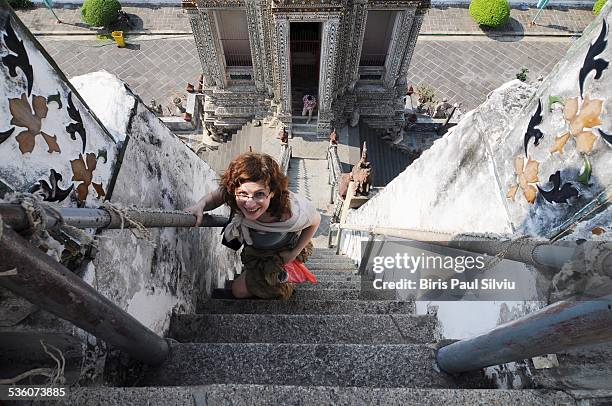 Young woman climbing the stairs at Wat Arun Temple, Bangkok, Thailand . Gigant ornate stupa rises over grounds of WatArun , Bangkok , Thailand