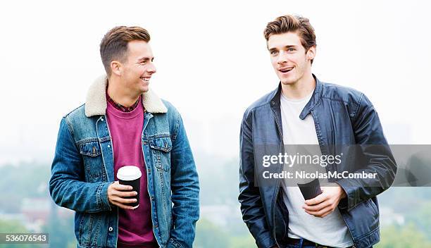 two young men in park discussing girls with coffee - only young men stock pictures, royalty-free photos & images