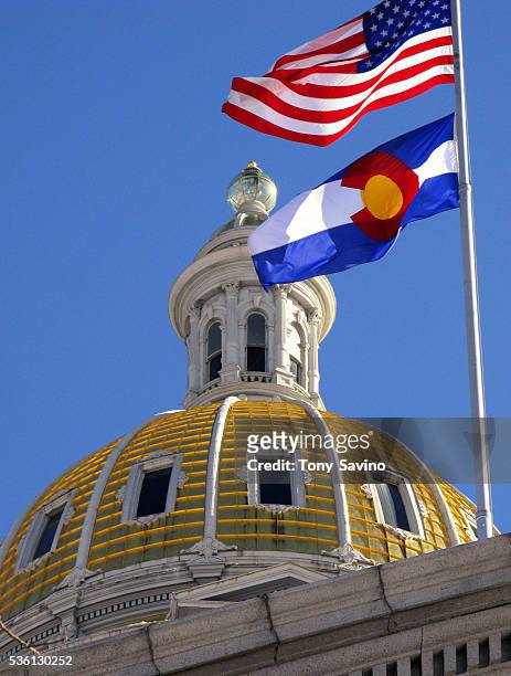 The United States and Colorado state flags fly near the gold dome of the State Capitol building.
