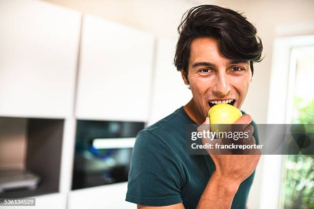 cheerful man eating an apple on kitchen - man biting apple stock pictures, royalty-free photos & images