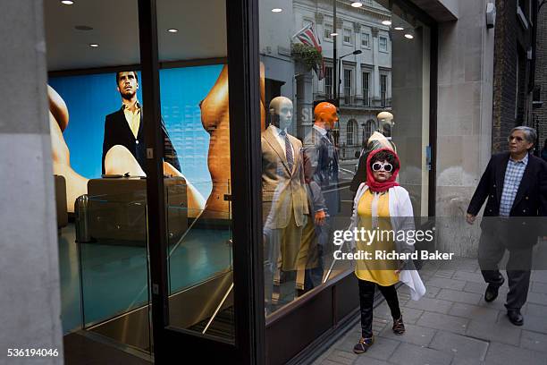 An eccentric looking woman passes-by Suitsupply, a fashion shop on Vigo Street in London's West End. Wearing large, owl-like glasses and a bright red...