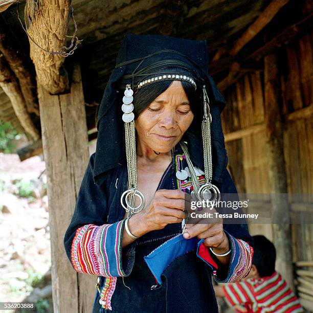 An Aini ethnic minority woman sewing her traditional clothing outside her home in Xiang Dao Ya village. Costume styles in the past were identified by...