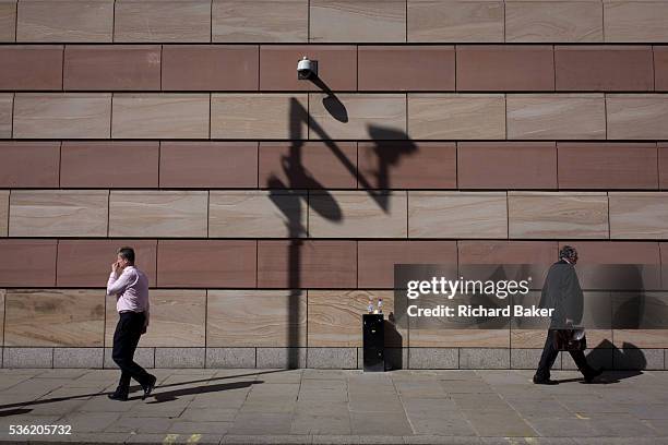 Businessmen pas each other below a CCTV camera with the shadow of a traffic camera on the wall of a modern office building in the City of London, the...