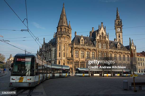 Modern De Lijn tramcar travels on the tram network past the historic building of the Old Post Office, Ghent, Belgium with a clear blue sky and...